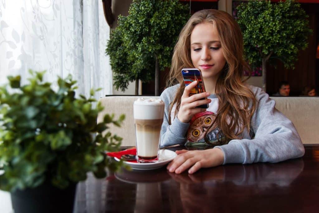 A woman sits in a cafe with her phone and a drink